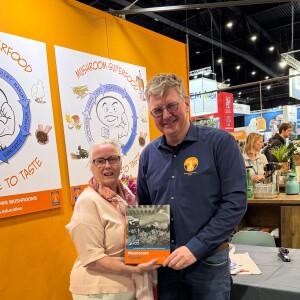 Mark den Ouden von Mushroom Office mit einem Vertreter von Agrar-Übersetzer auf den Dutch Mushroom Days 2026, mit dem Buch Mushroom Signals im Bild.